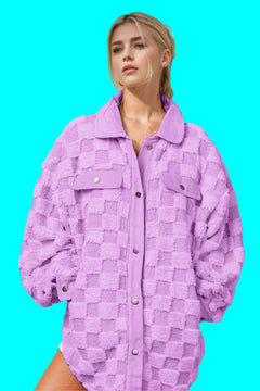 This image features a young woman posing in a striking lavender textured jacket against a neutral backdrop with a dynamic light and shadow play. The jacket has a fluffy, patch-like texture with a button-up front and prominent collar. Her blonde hair is styled in a neat updo, and she has a soft makeup look, gazing off to the side, which adds an introspective quality to the photo. The overall styling and color palette give the image a fresh, contemporary feel.